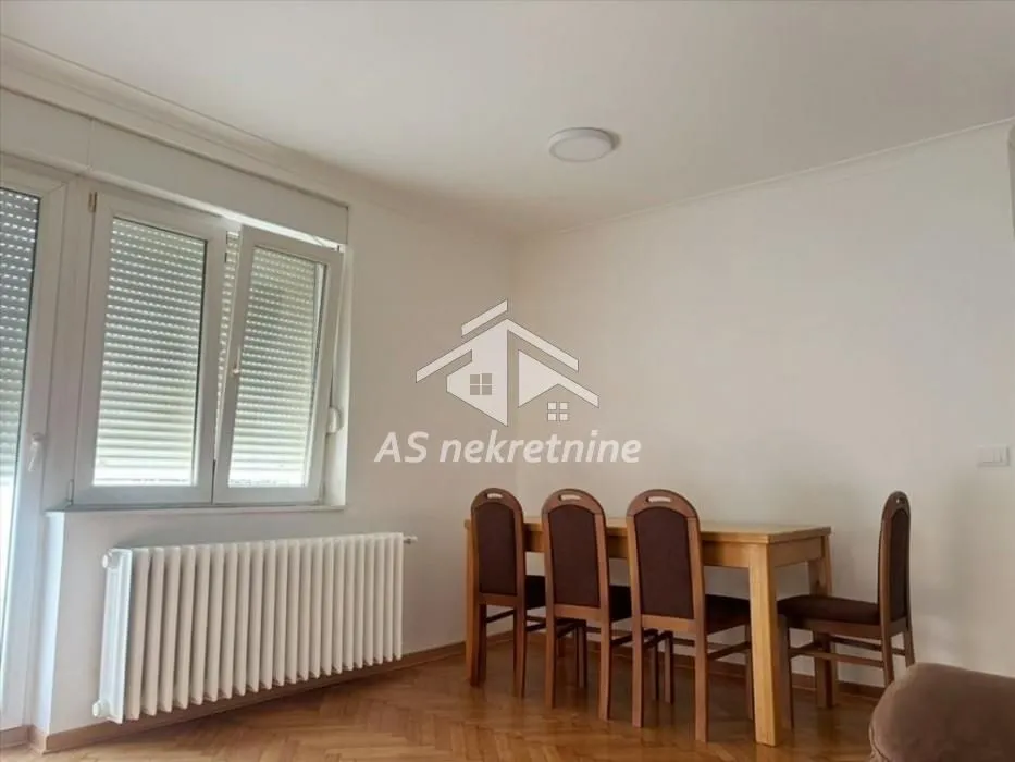 Dining area with a wooden table and chairs in a bright room with windows.