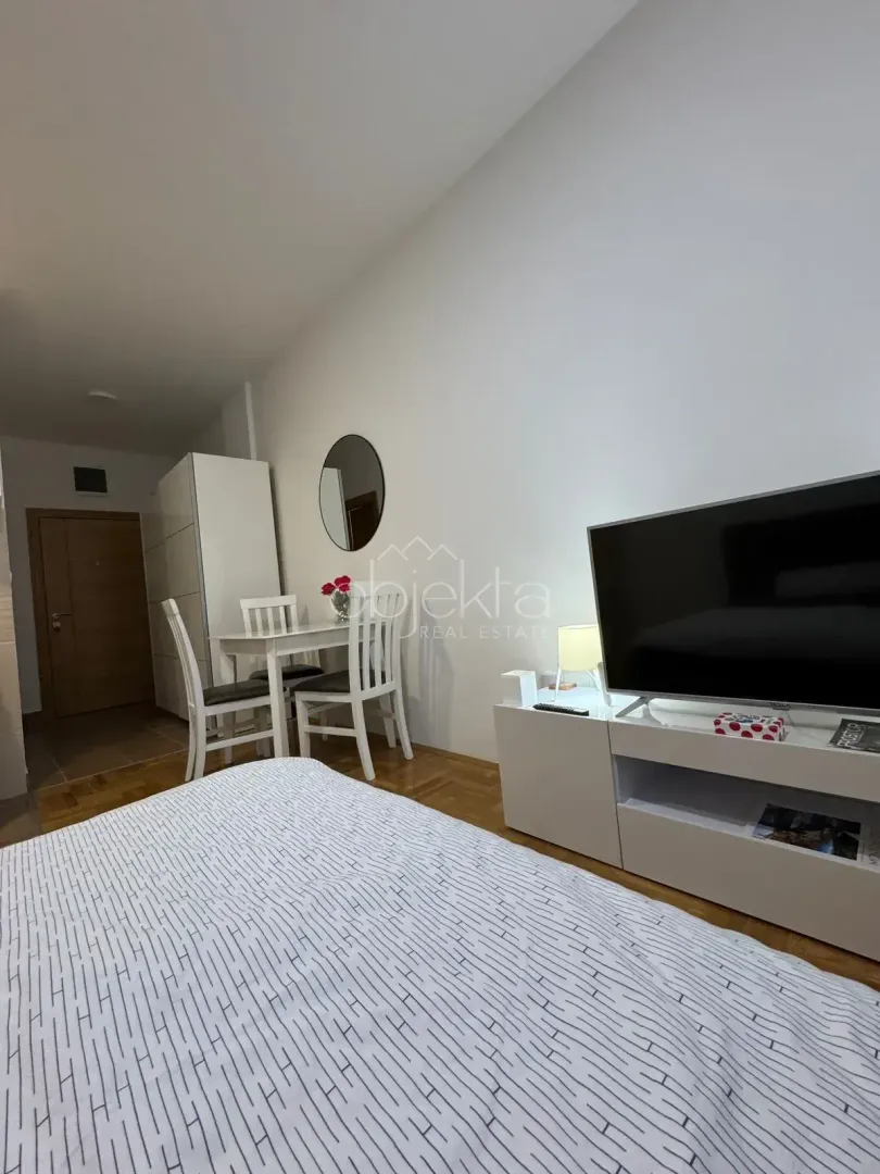 Furnished bedroom with a bed, TV, and a small dining table.