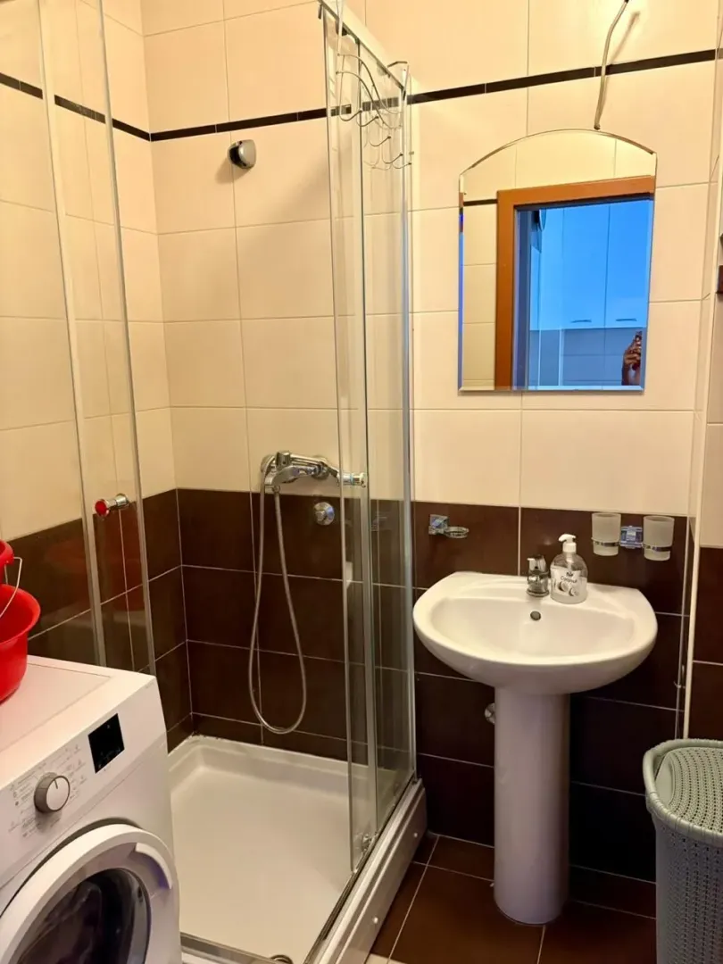 Bathroom with a shower cabin, sink, mirror, and washing machine.