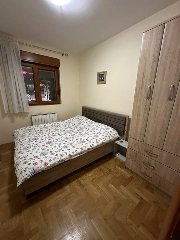 Namještena spavaća soba sa bračnim krevetom i drvenim ormarom.
