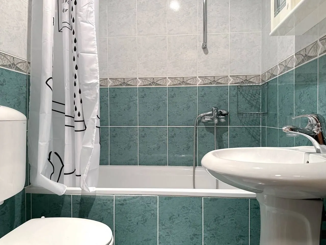 Smaller bathroom with a bathtub, washbasin, and toilet bowl tiled with ceramic tiles.