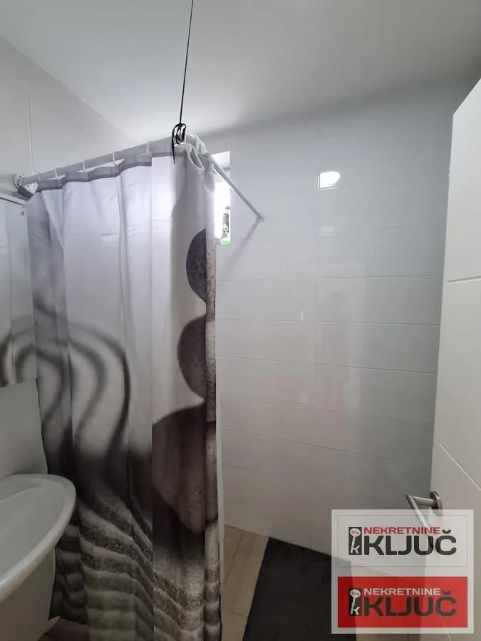 Kupatilo sa tuš kabinom i belim pločicama.