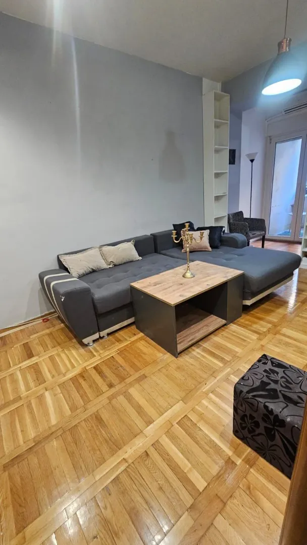 Dnevna soba sa ugaonom garniturom, stočićem i drvenim parketom.