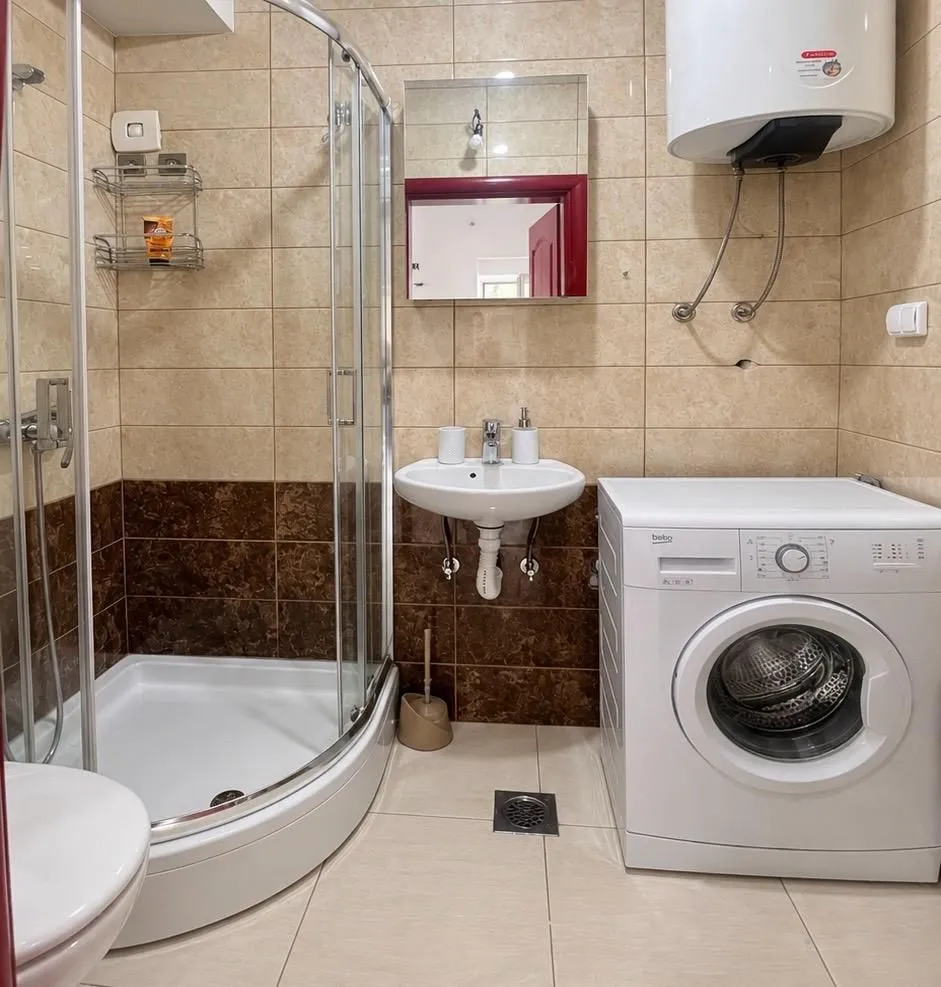 Small bathroom with a shower cabin, washbasin, and washing machine.