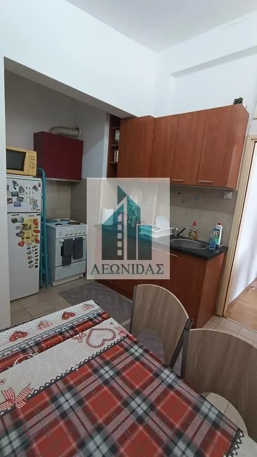 Small kitchen with wooden cabinetry and a dining table in the foreground.