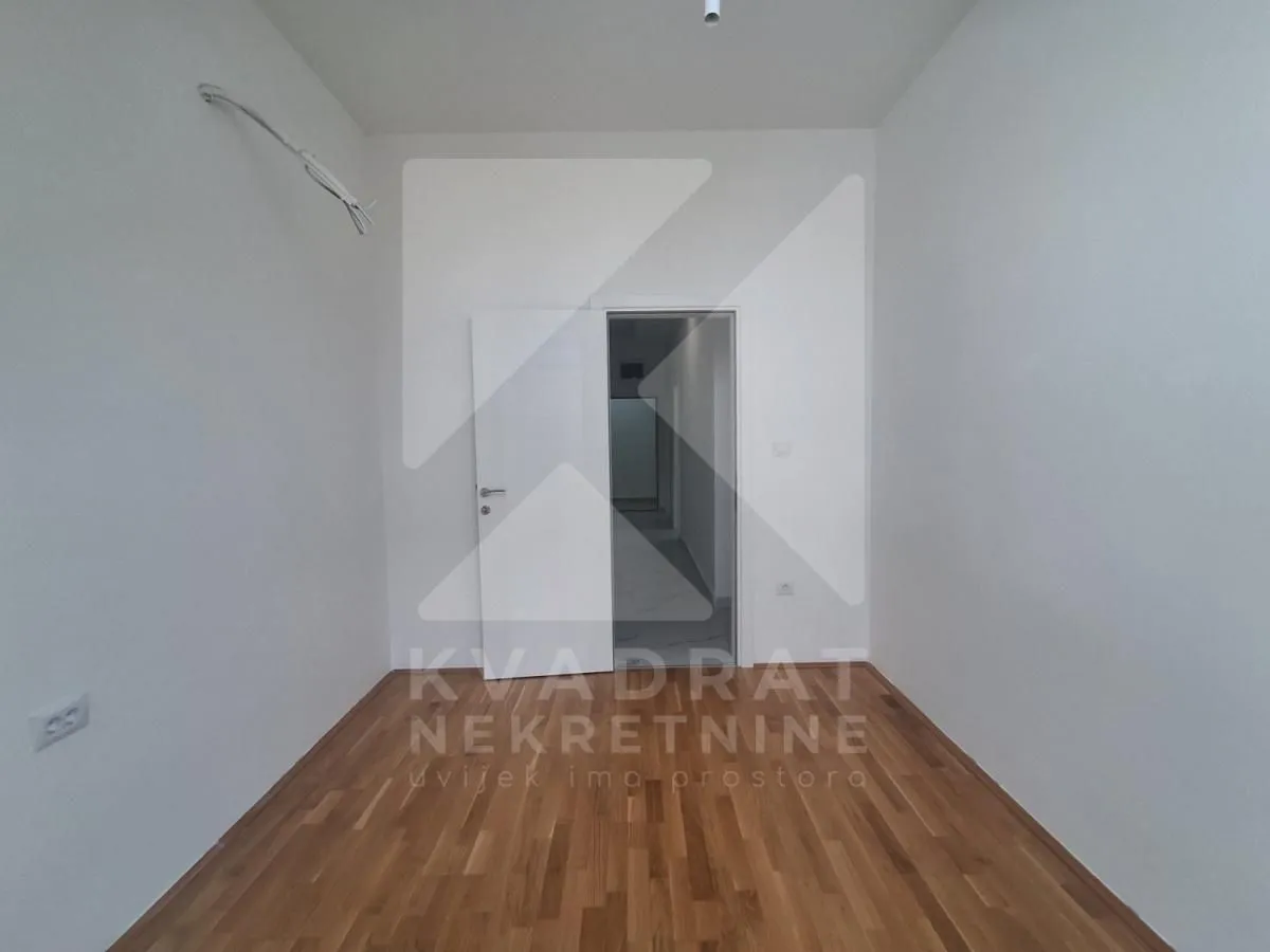 Prazna prostorija sa drvenim podom i otvorenim vratima.
