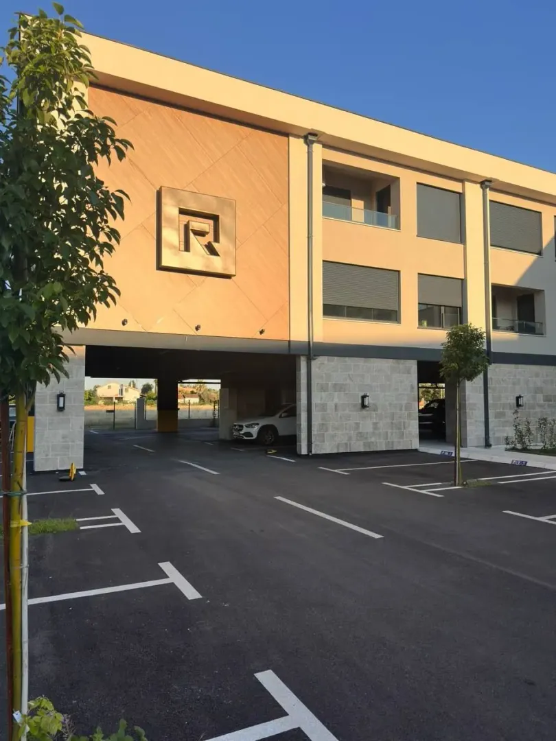 Pogled na spoljašnjost zgrade sa parkingom i ulazom u garažu.