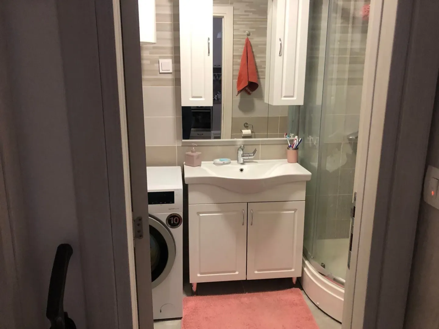 View of the bathroom with a sink, mirror, shower cabin, and washing machine.