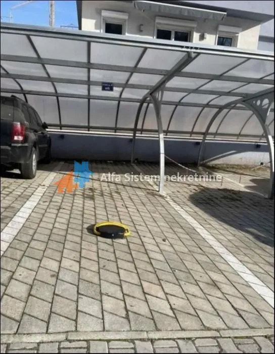 Natkriveni parking prostor sa popločanim podom i parkiranim automobilom.