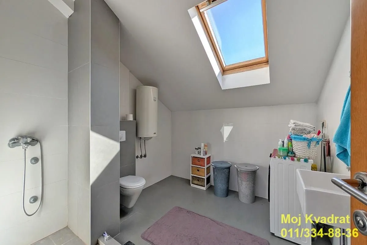 Attic bathroom with a skylight, shower cabin, toilet, and washing machine.