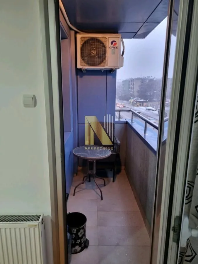 Manji zatvoreni balkon sa stolom, stolicama i klima uređajem.