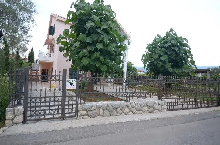 Vanjski dio kuće sa ograđenim dvorištem i drvećem.