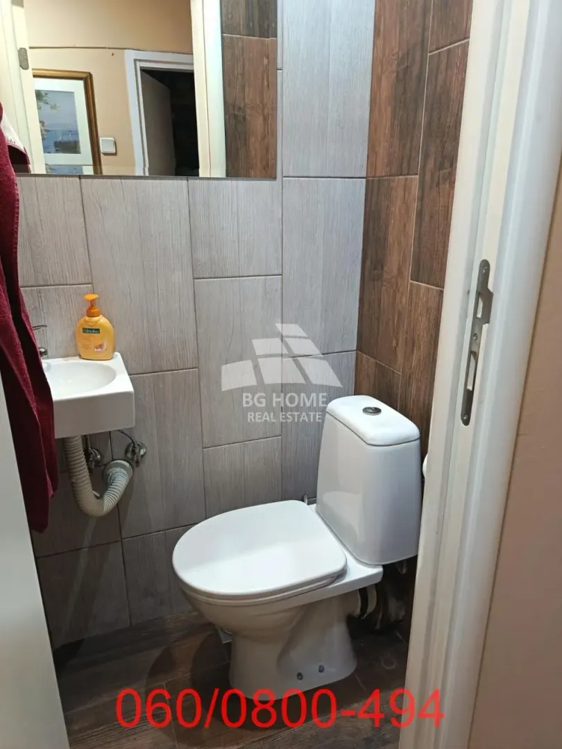 Manje kupatilo sa wc šoljom i umivaonikom, obloženo keramičkim pločicama.