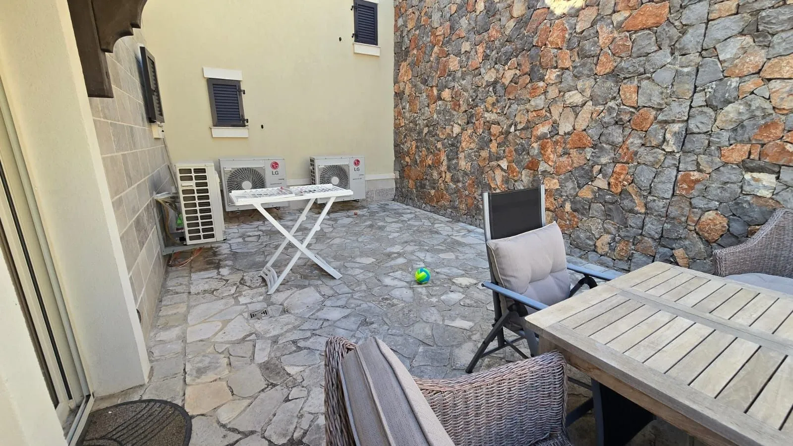 Dvorište popločano kamenom sa prostorom za sjedenje i klima uređajima.