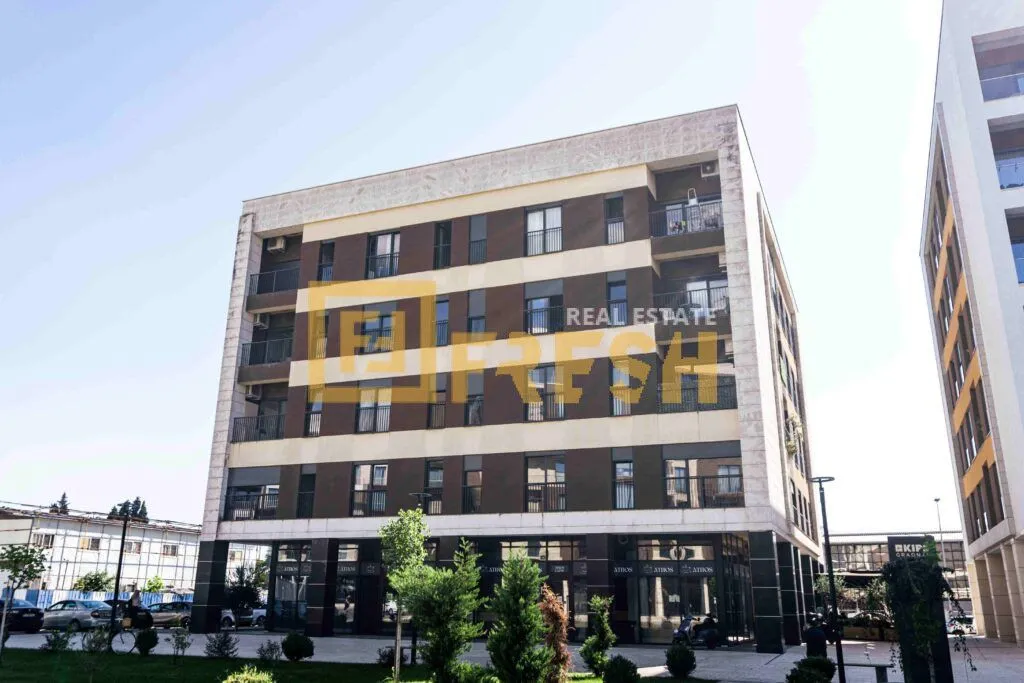 Exterior view of a modern residential building with balconies and commercial space on the ground floor.