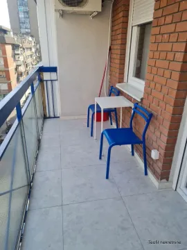Narrow tiled balcony with a white table, blue chairs, and a street view. - image 7
