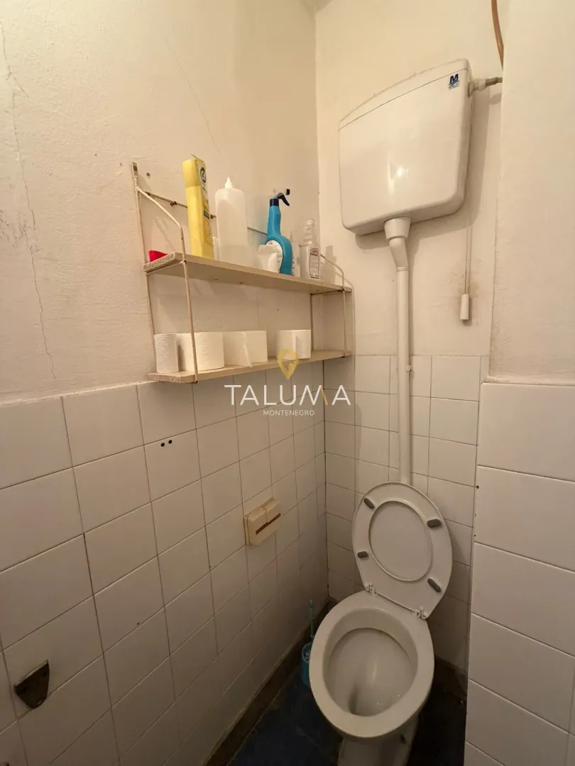 Manje kupatilo sa wc šoljom i zidnom policom sa higijenskim potrepštinama.