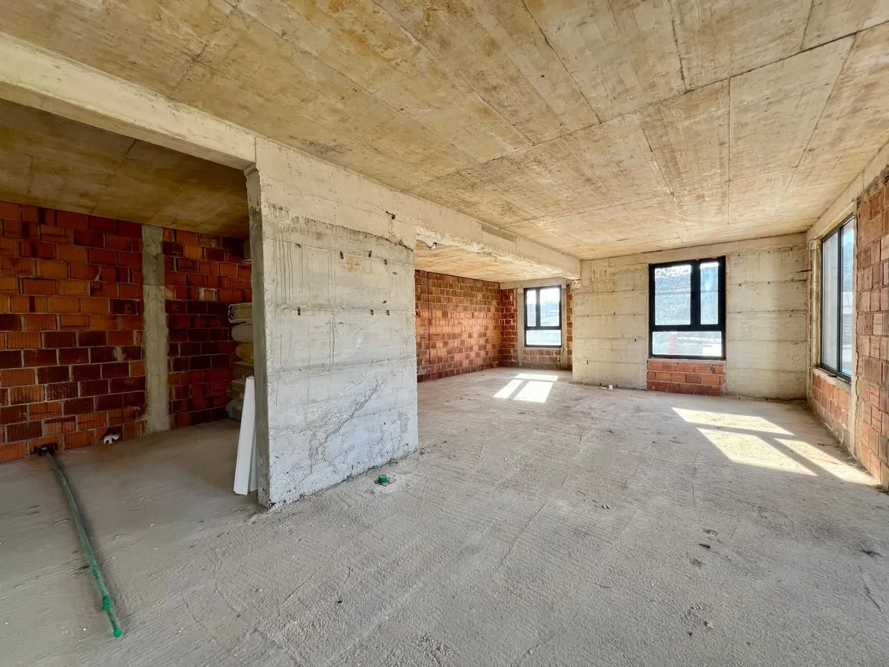 Interior of an unfinished apartment in grey phase with concrete pillars and windows.