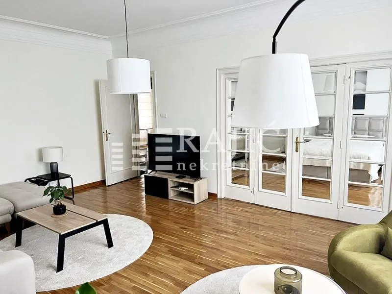 Spacious living room with wooden flooring, modern furniture, and a dining area in the background.
