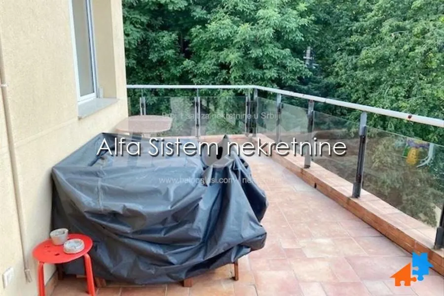 Prostrana terasa sa staklenom ogradom i pogledom na zelenilo.