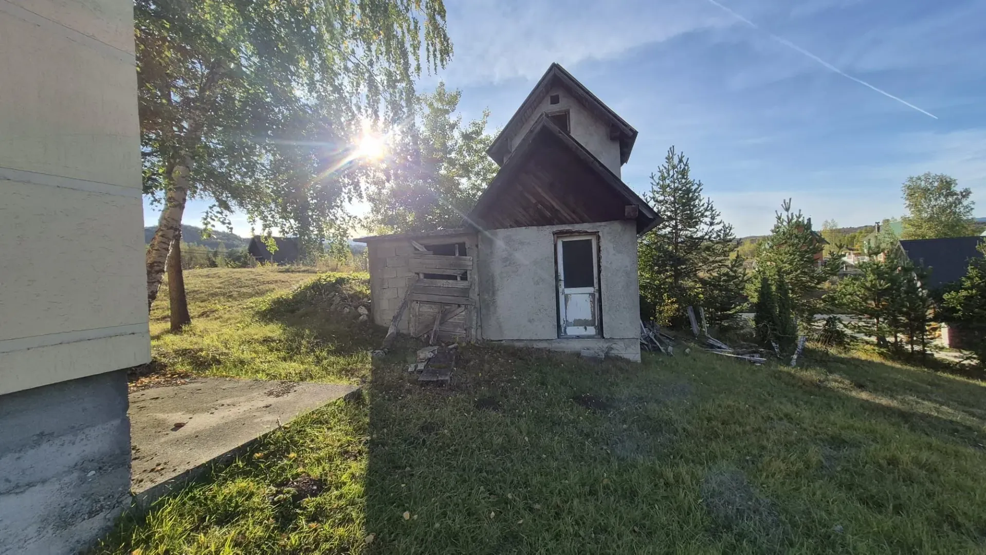 Eksterijer manje kuće sa dvorištem i drvećem.