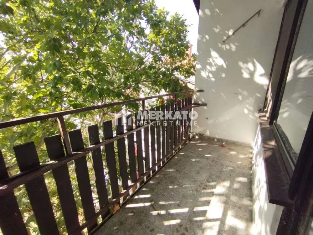 Manji balkon sa drvenom ogradom i pogledom na zelenilo.