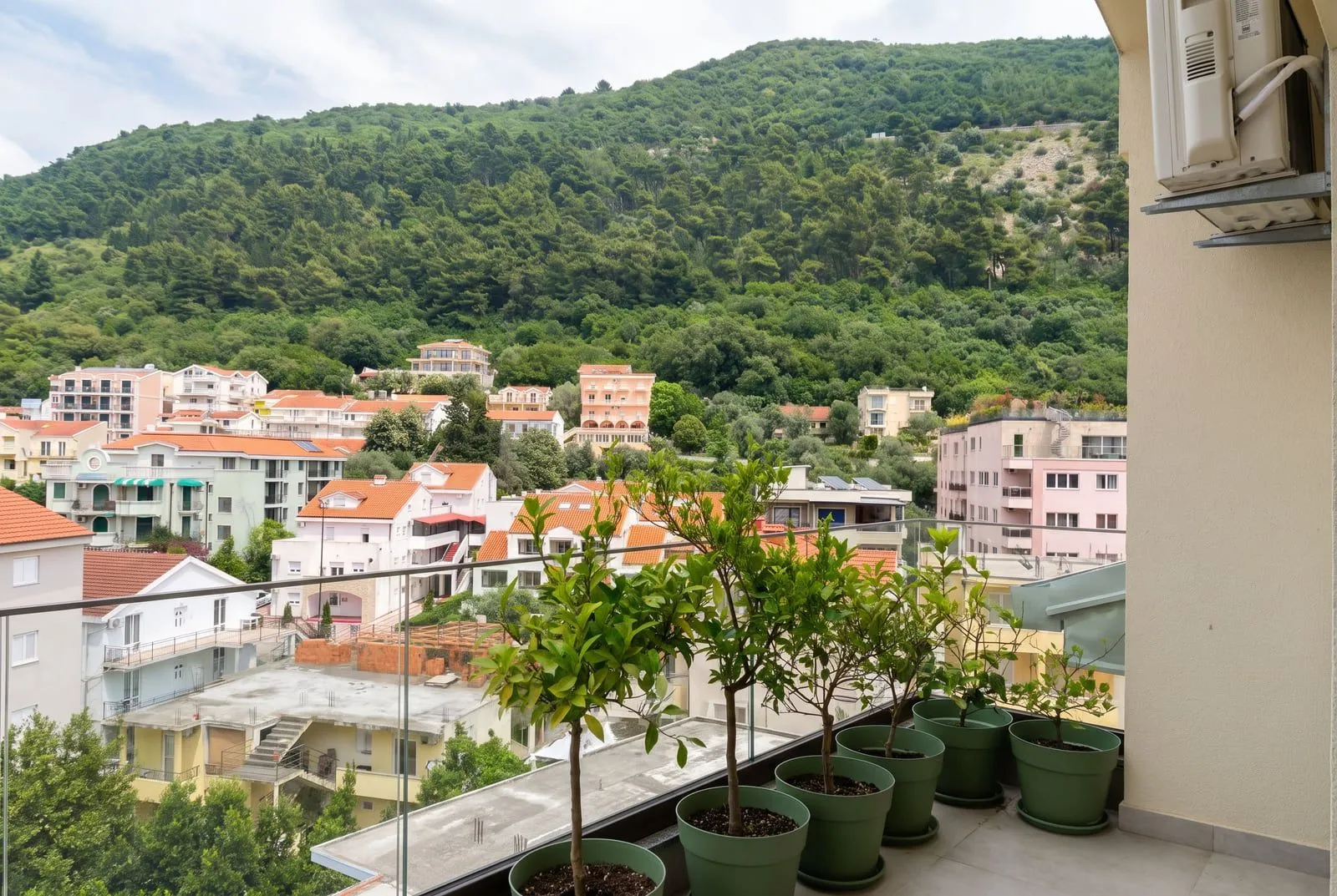 Pogled sa balkona na okolne zgrade, zelenilo i brdo.