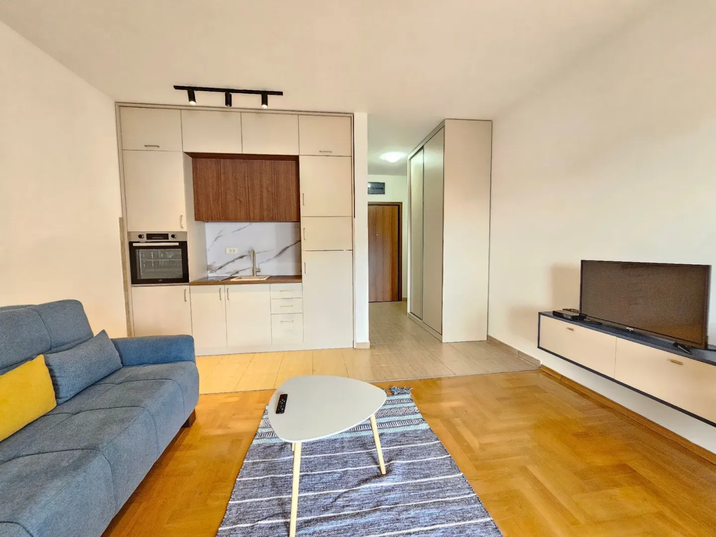 Living room with a sofa, television, and integrated kitchen.