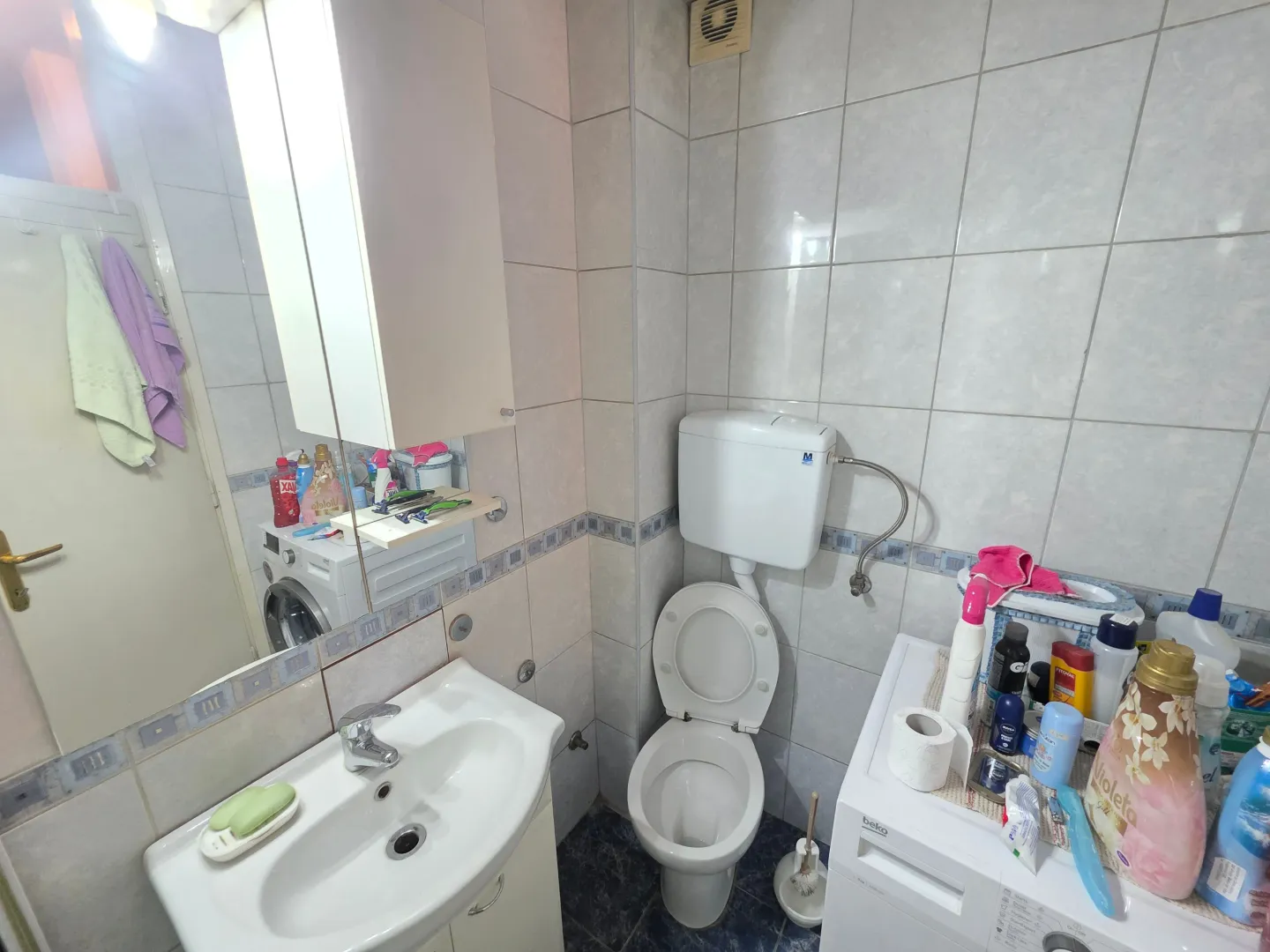 Manje opremljeno kupatilo sa umivaonikom, WC šoljom i veš mašinom.