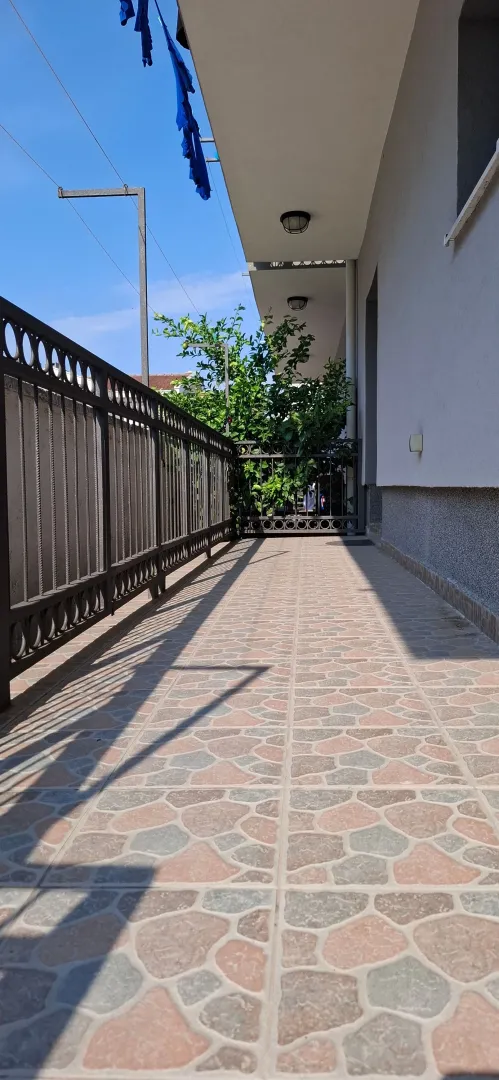 Prostrana terasa sa pločicama i metalnom ogradom.