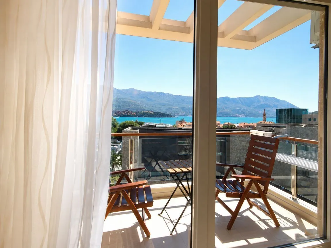 Sea and mountain view from a furnished balcony featuring a wooden table and chairs.