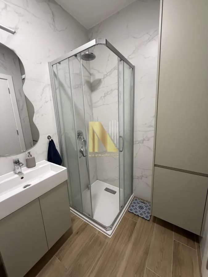 Moderno kupatilo sa tuš kabinom, umivaonikom i ogledalom.