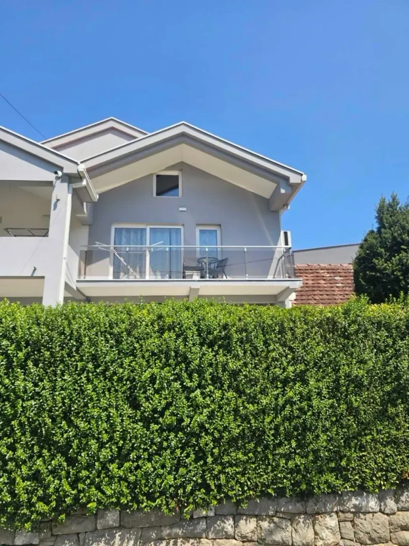 Exterior view of the house with a balcony and a neat hedge in the yard.
