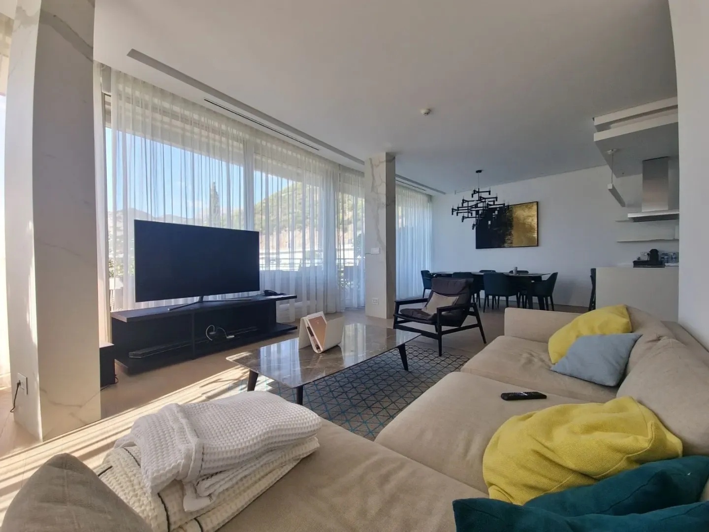 Spacious living room connected to the dining area and kitchen, featuring large windows and a TV.