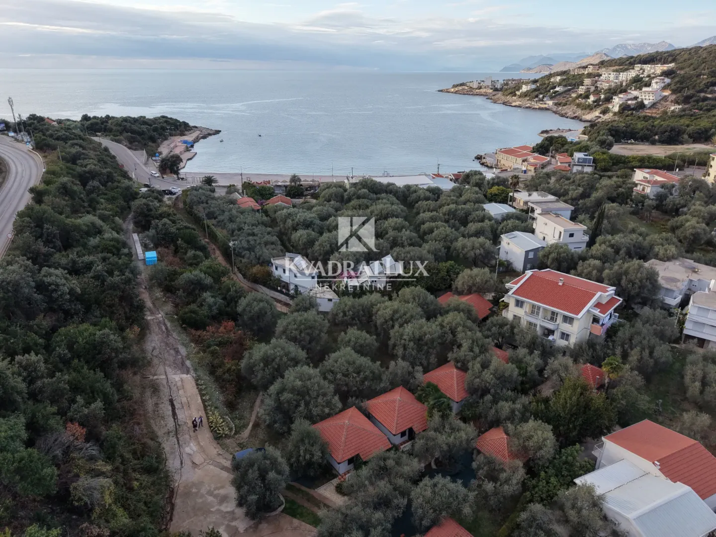 Pogled iz vazduha na obalu mora i okolno naselje sa zelenilom.