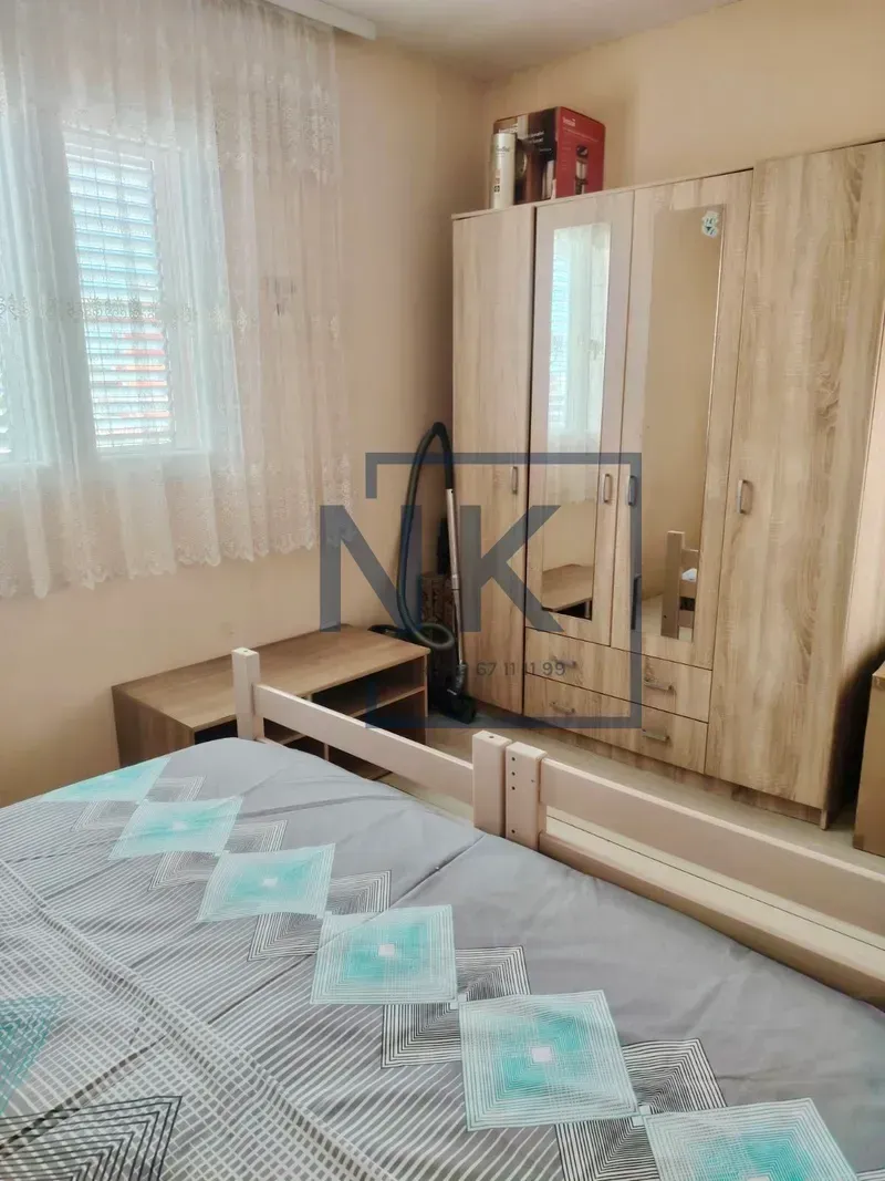 Bedroom with a bed, a large wooden wardrobe, and a window with curtains.