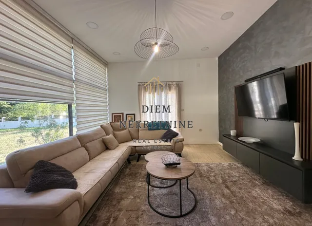 Modern and bright living room with a corner sofa, TV unit, and large windows.