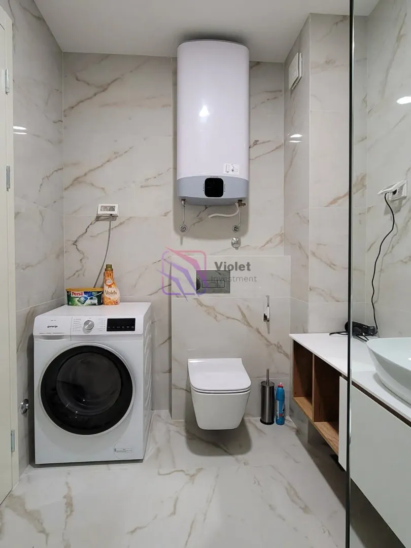 Moderno opremljeno kupatilo sa veš mašinom, WC šoljom i umivaonikom.
