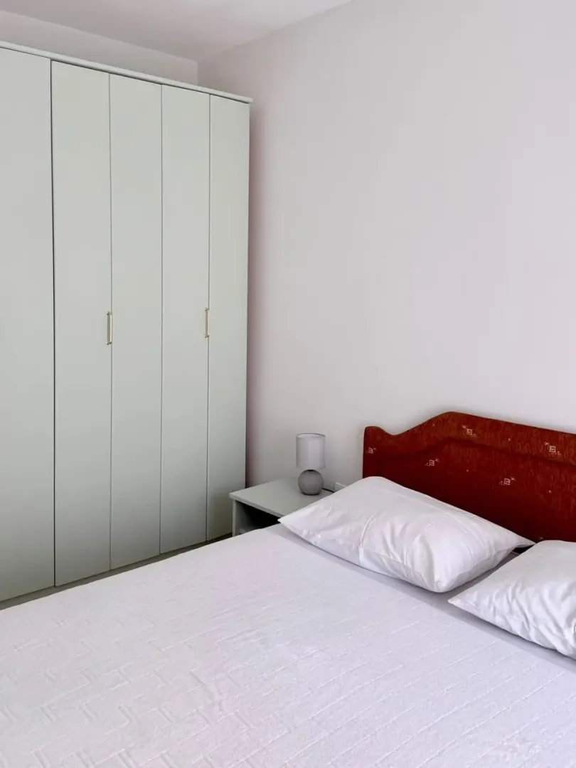 Furnished bedroom with a double bed, wardrobe, and a bedside table with a lamp.