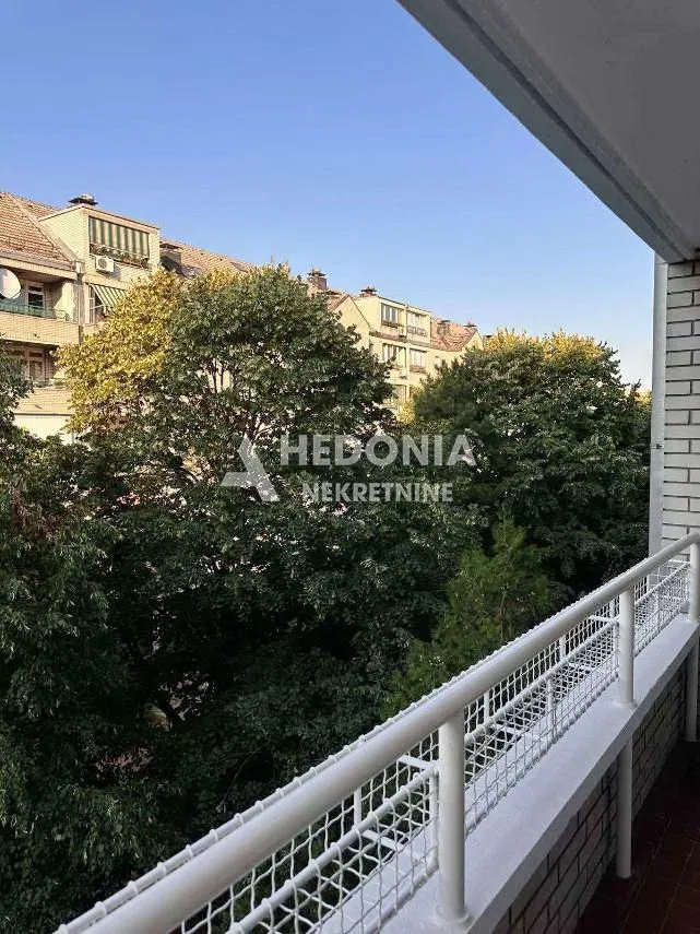 Pogled sa balkona na zeleno drveće i okolne zgrade.