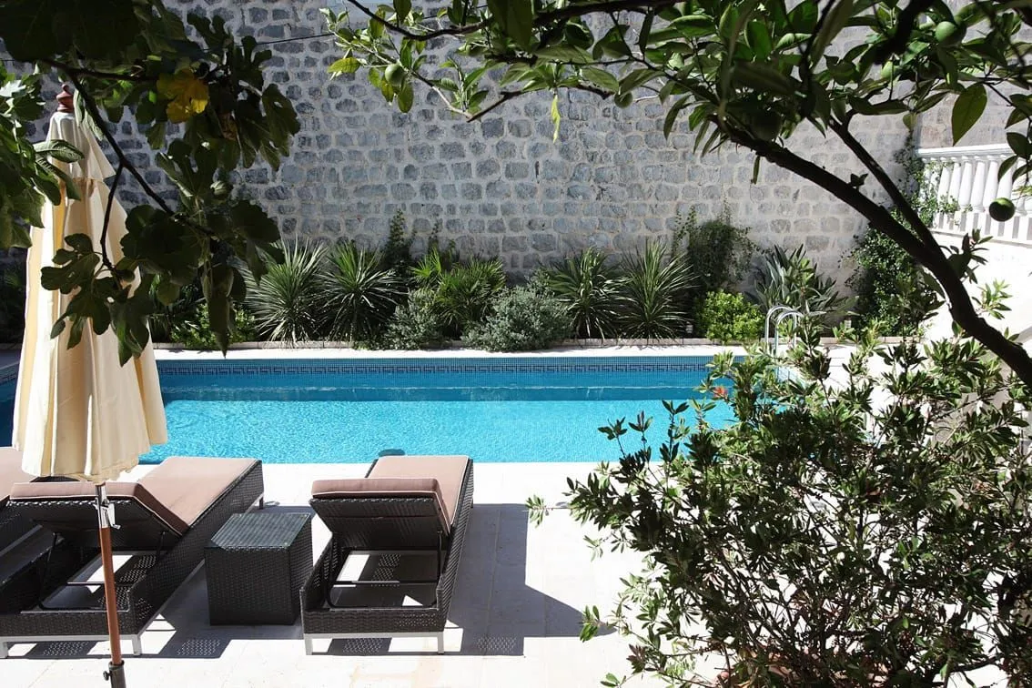 Yard with a swimming pool and sun loungers in front of a stone house.