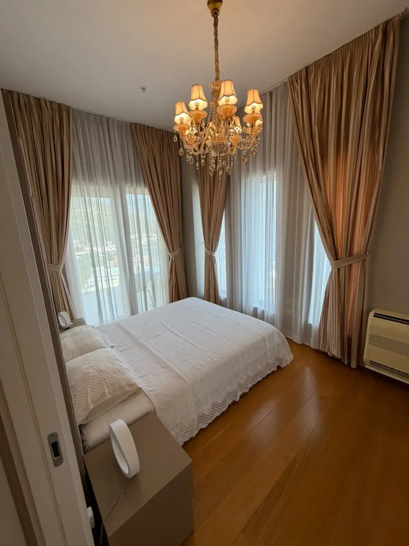 Bedroom with a double bed, wooden flooring, and large windows with curtains.