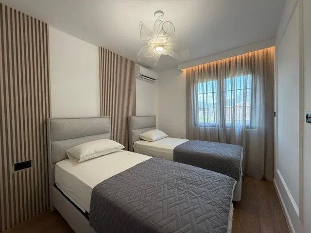 Moderna spavaća soba sa dva singl kreveta i dekorativnim drvenim panelima.