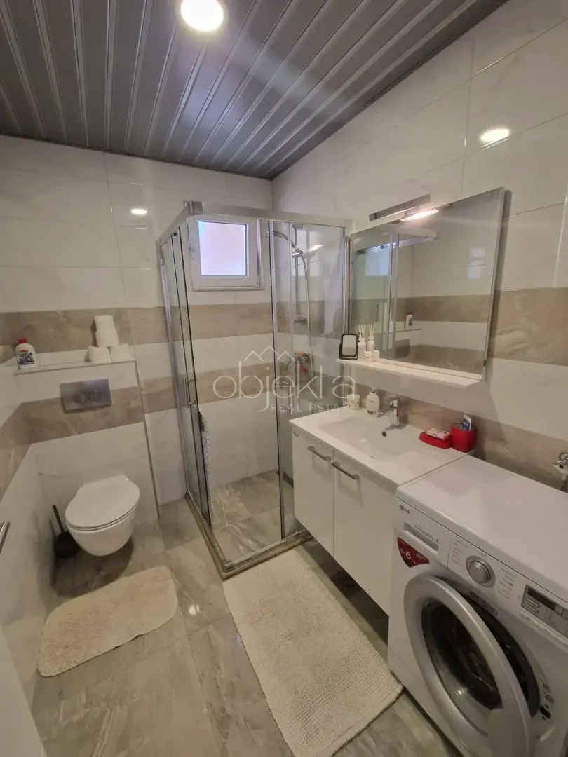 A modern bathroom equipped with a shower cabin, vanity unit, and washing machine.
