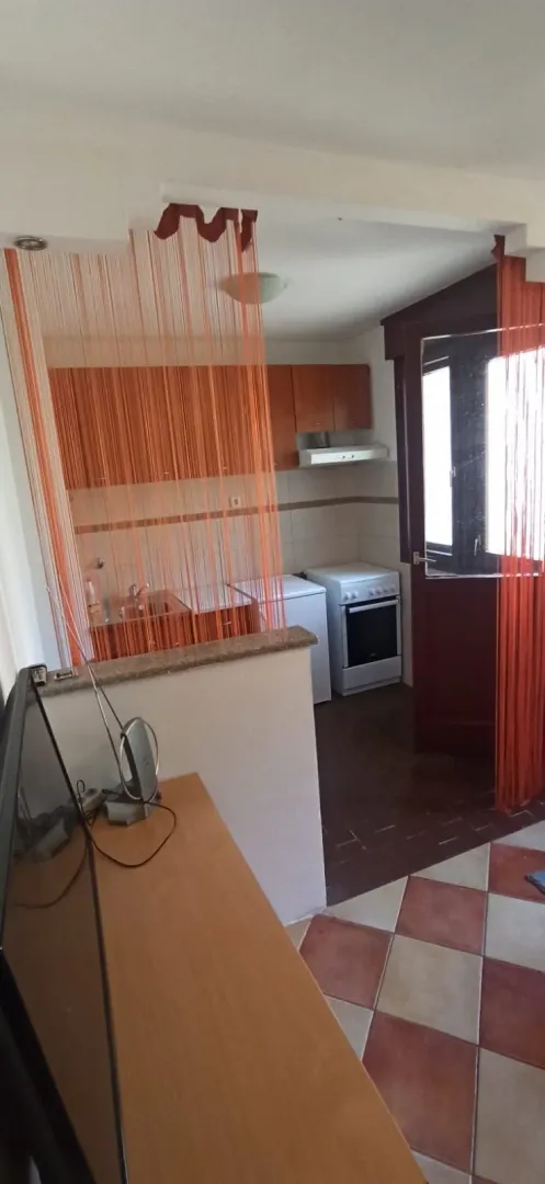 Manja kuhinja odvojena od dnevnog boravka narandžastim nitastim zavjesama.