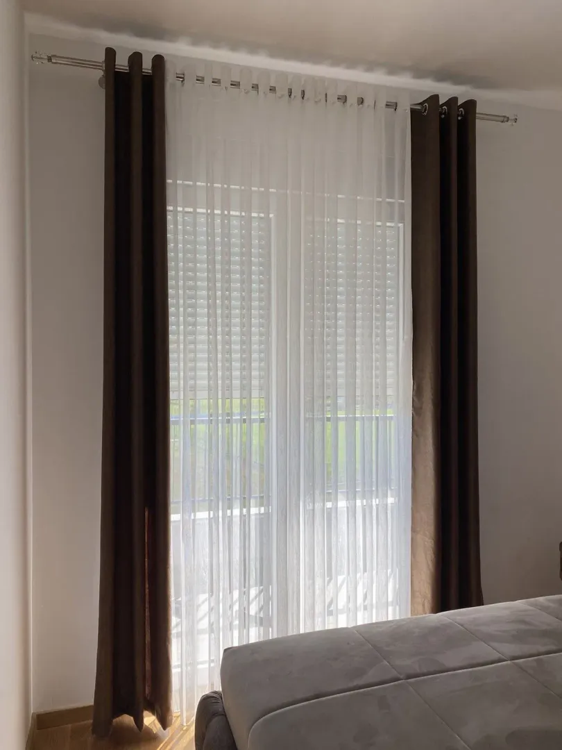 A bright window with curtains and part of a bed.