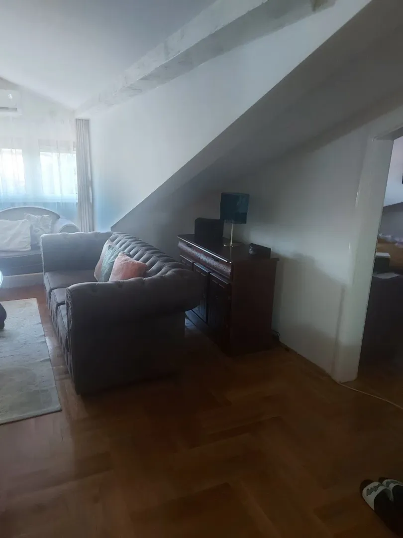 Dnevna soba u potkrovlju sa udobnim dvosjedom i drvenom komodom ispod kosine.
