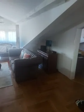 Dnevna soba u potkrovlju sa udobnim dvosjedom i drvenom komodom ispod kosine. - image 6