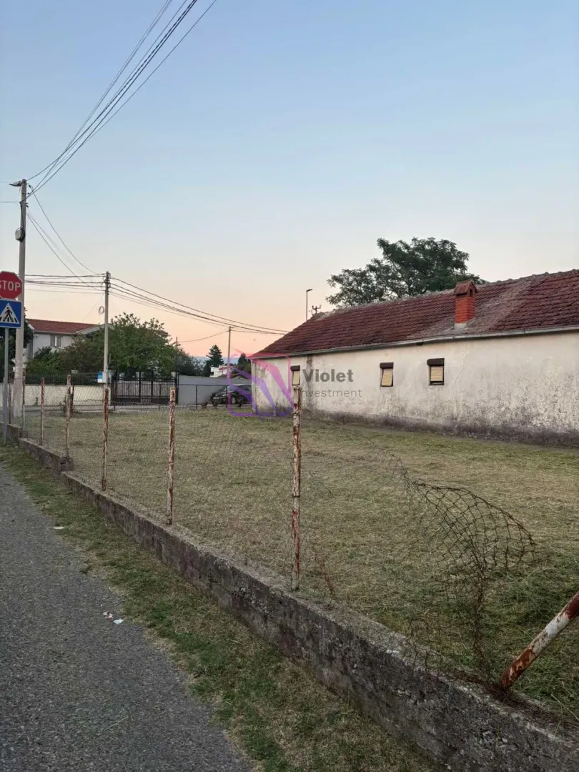 Pogled na plac sa travnatom površinom i ogradom ispred pomoćnog objekta.
