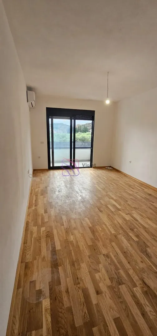 Prazna prostorija sa drvenim parketom i izlazom na terasu.